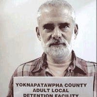 Melvin Roberts Older man with white hair, mustache and beard holding a jail booking card